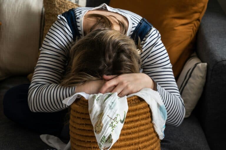erschöpfte Frau über einem Wäschekorb - Jetlag mit Kindern: was hilft?