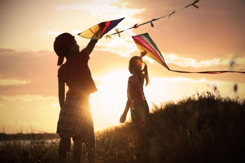 Kinder spielen im Sonnenuntergang mit Drachen. Was brauchen Kinder, um glücklich zu sein?