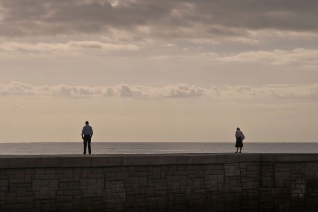 zwei Personen stehen auf einer Mauer am Meer, mit einer grossen Distanz dazwischen. Konflikte zwischen erwachsenen Kindern und Eltern sind sehr belastend.