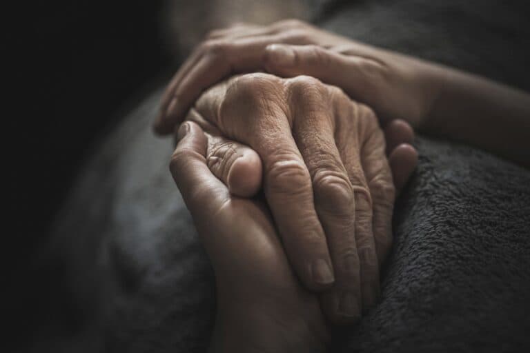 Zwei Hände halten die Hand einer älteren Person. Wenn zur Betreuung der Kinder die Pflege der eigenen Eltern kommt, ist die Belastung gross.
