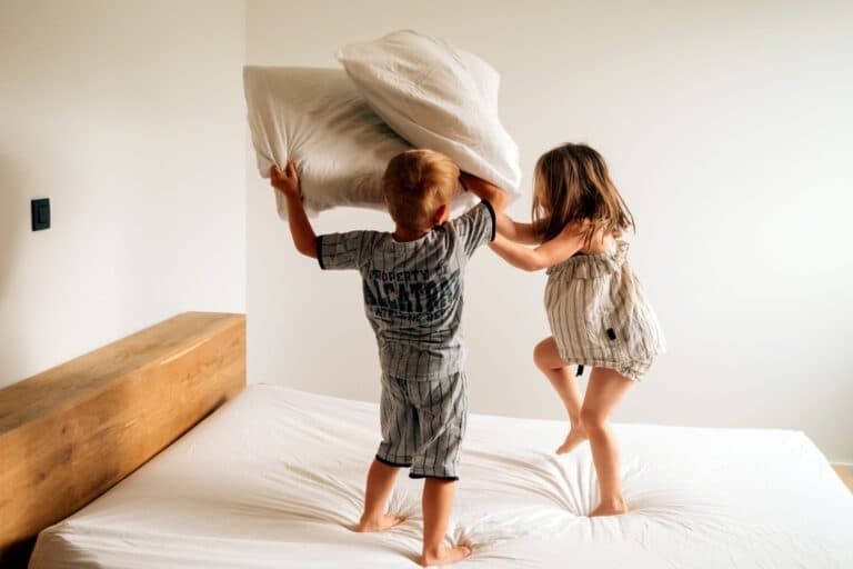 Kinder die sich auf dem Bett eine Kissenschlacht liefern. Kinder streiten, um Beziehungspflege und Konfliktschule zu betreiben. Eltern, lasst sie!