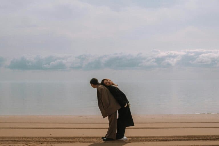 zwei Personen im Sand stehend, die sich aufeinander abstützen. Ist Monogamie wirklich die passende Beziehungsform, die glücklich macht?