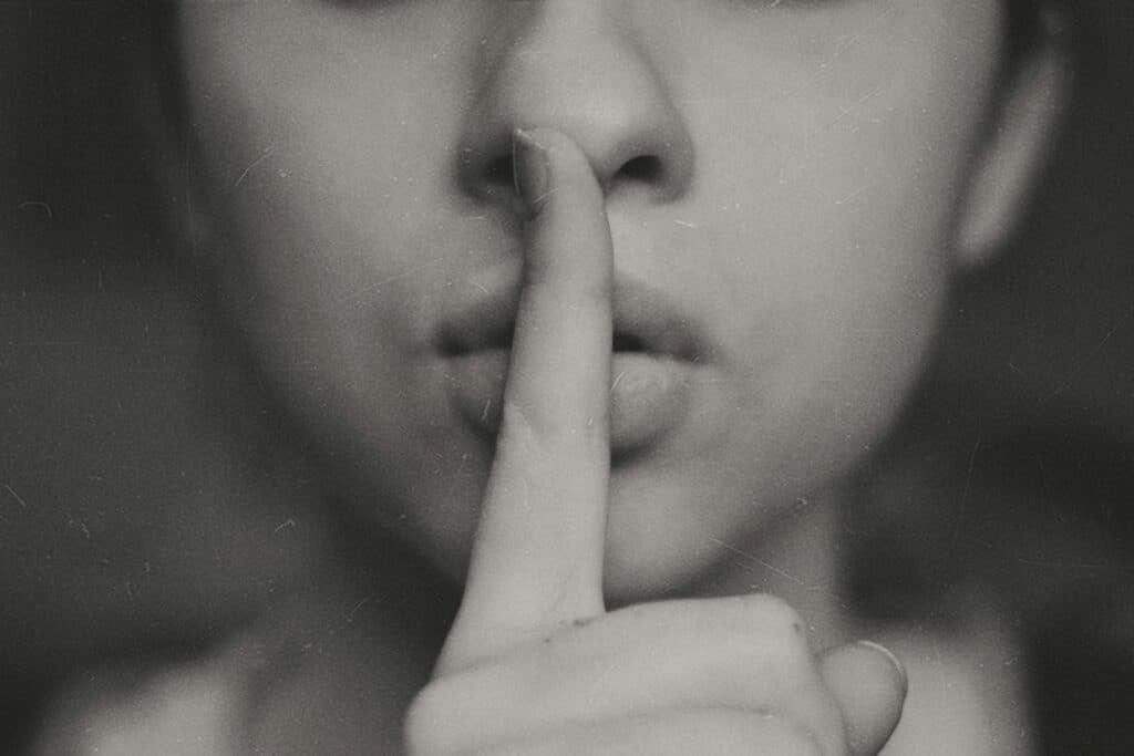 Person hält sich den Finger an die Lippen, als Symbol für leise sein oder Geheimnis.
