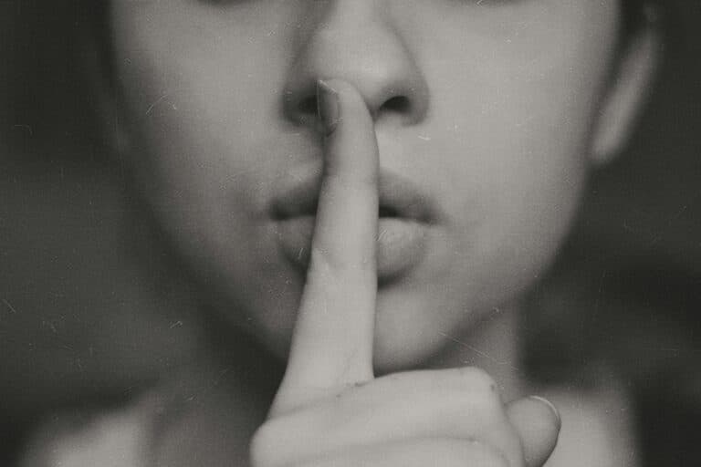 Person hält sich den Finger an die Lippen, als Symbol für leise sein oder Geheimnis.