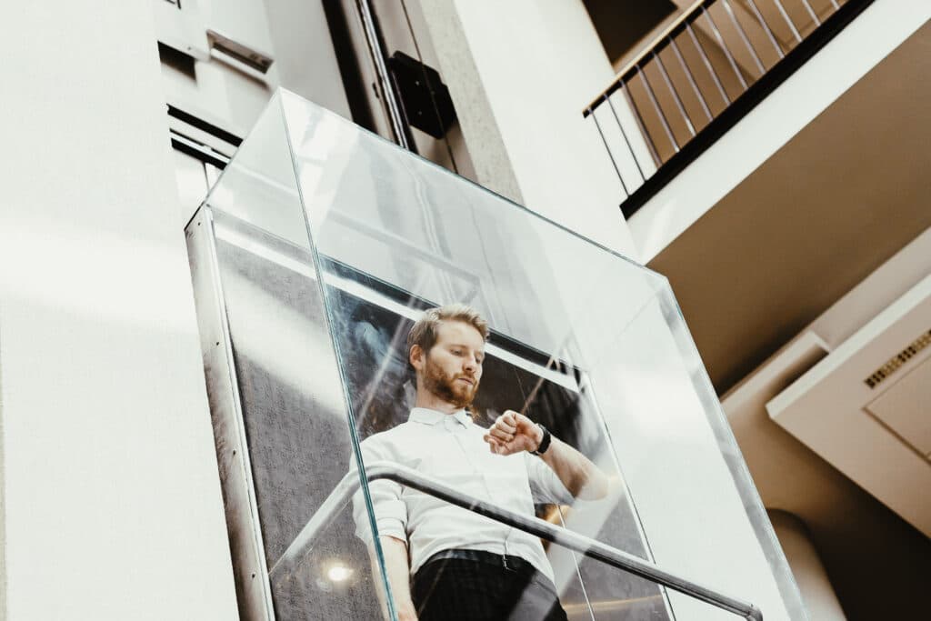 Mann steht in einem Lift und schaut auf seine Uhr. Remote Work und Homeoffice sind für viele Väter wichtig.