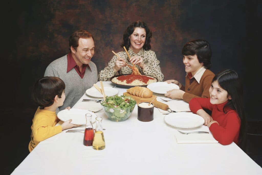 Familie sitzt am Esstisch bei Spaghetti und Salat, alle lächeln unnatürlich. Wieso spielt man als Familie heile Welt, auch nach einer Trennung?