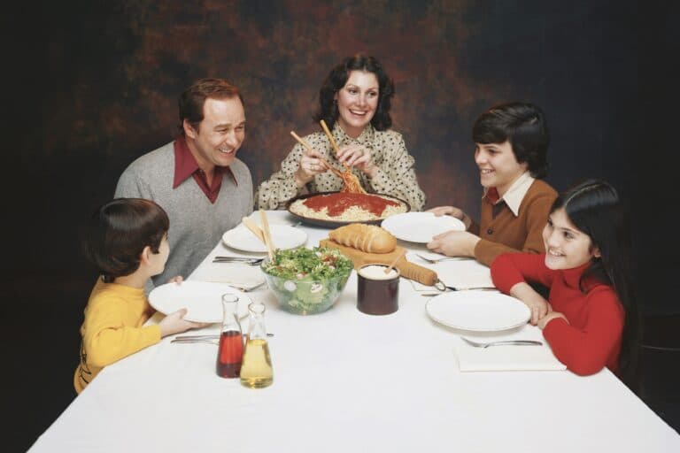 Familie sitzt am Esstisch bei Spaghetti und Salat, alle lächeln unnatürlich. Wieso spielt man als Familie heile Welt, auch nach einer Trennung?