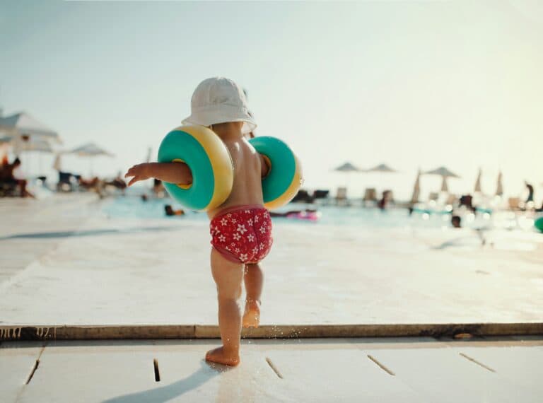 Kind steht an Poolrand mit Schwimmflügel. Unaufmerksamkeit kann schnell zum Ertrinken führen