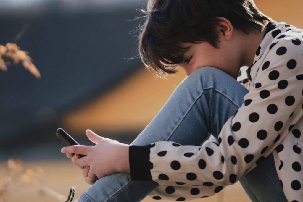 Kind blickt auf ein Smartphone - Medienkonsum von Kindern und Jugendlichen ist für Eltern oft schwierig zu kontrollieren