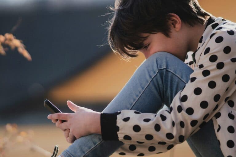 Kind blickt auf ein Smartphone - Medienkonsum von Kindern und Jugendlichen ist für Eltern oft schwierig zu kontrollieren
