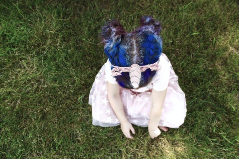 Kind mit Kleid und buntem Haar spielt in der Wiese