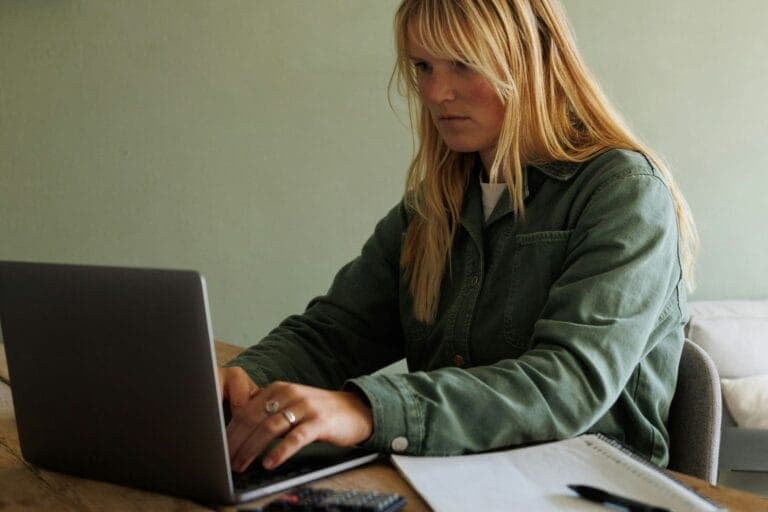 Eine Frau sitzt mit einem Taschenrechner vor ihrem Computer und tippt.