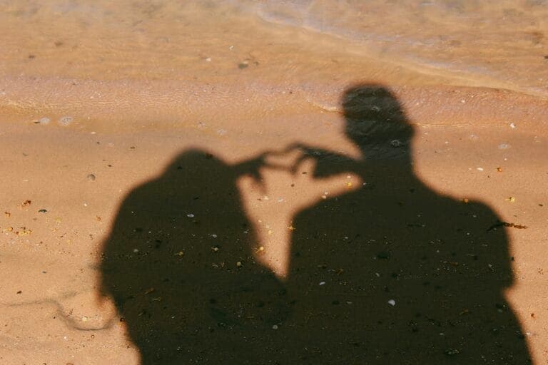 Ein Paar formt ein Herz mit den Händen. Ihr Schatten ist in der Sonne zu sehen.