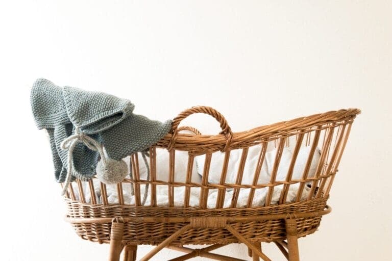 Babykorb mit darüber hängender Strickmütze und -kleidung. - Erstausstattung fürs Baby: Welche Produkte brauchen wir wirklich?