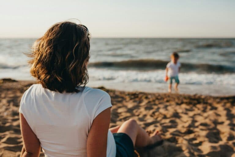 Frau sitzt am Meer und sieht ihrem Kleinkind beim Spielen zu - Alleinerziehend zu sein, kann auch schöne Seiten und Vorteile haben