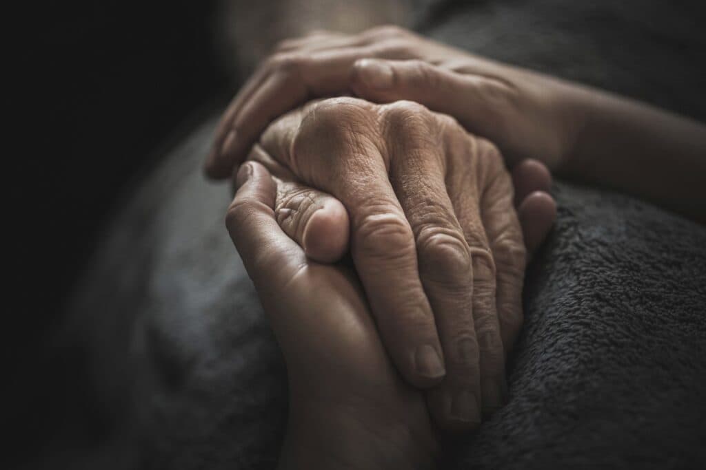 Zwei Hände halten die Hand einer älteren Person. Wenn zur Betreuung der Kinder die Pflege der eigenen Eltern kommt, ist die Belastung gross.