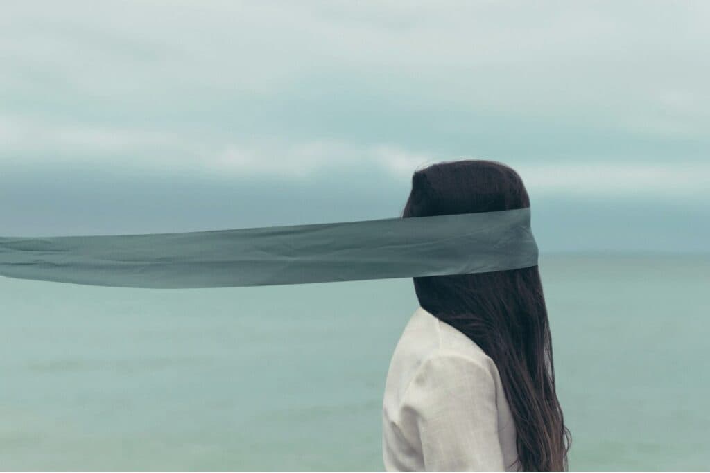 Frau steht am Meer, die Augen mit einem Tuch verbunden. Als Marah Rikli früh in die Wechseljahre kommt, nimmt niemand ihre Symptome ernst.