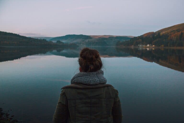 Frau steht an einem See, sie ist nur von hinten zu sehen. Wie fühlt es sich an, wenn man die Mutterschaft bereut?