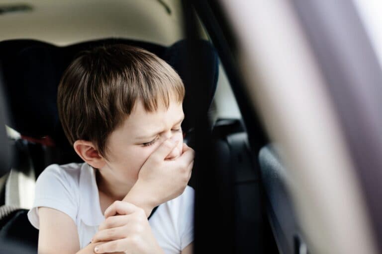 Kind im Auto, das sich die Hand vor den Mund hält - Reiseübelkeit - Tipps für die Fahrt in die Ferien mit Kindern