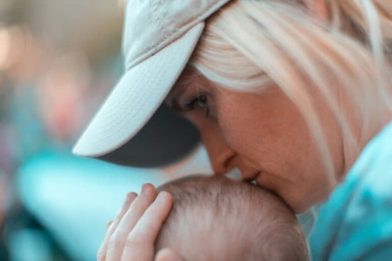 Frau mit nachdenklichem Blick küsst Babykopf. Kein Partner, aber ein grosser Kinderwunsch? Erfahrungsbericht einer Single Mom by Choice.