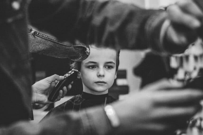 Mädchen im Schulalter mit traurigen Blick, dem die Haare abrasiert werden