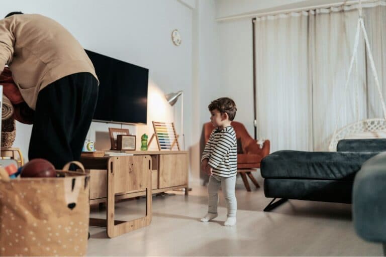 Kleinkind steht im Wohnzimmer und schaut zu, wie der Vater aufräumt. - Überblick über Wohn- und Betreuungsmodelle nach einer Trennung