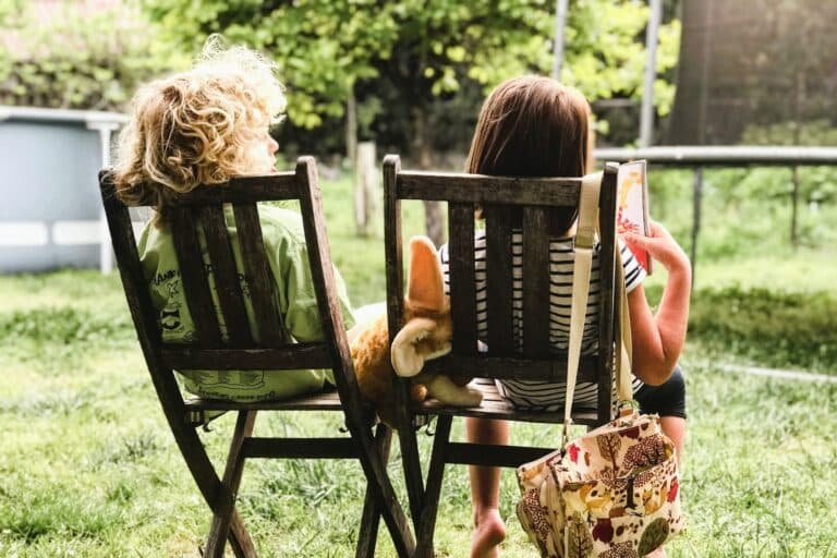 Zwei Kinder sitzen auf Stühlen und schauen ein Bilderbuch an. Freundschaften sind sehr wichtig für Kinder.