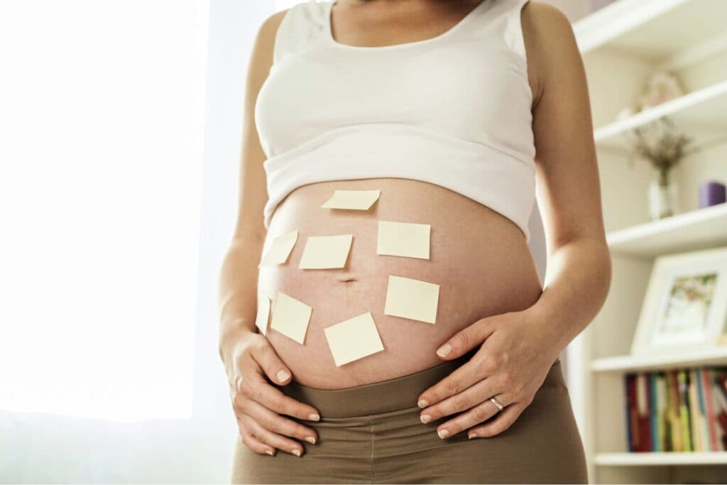 Bauch einer schwangeren Frau mit vielen Post-it-Zetteln. – Ist man schwanger, lassen die ungebetenen Ratschläge nicht lange auf sich warten.
