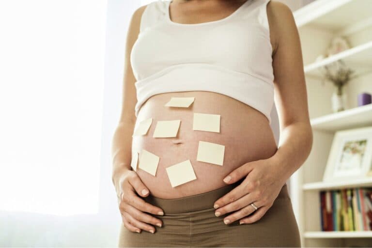 Bauch einer schwangeren Frau mit vielen Post-it-Zetteln. – Ist man schwanger, lassen die ungebetenen Ratschläge nicht lange auf sich warten.