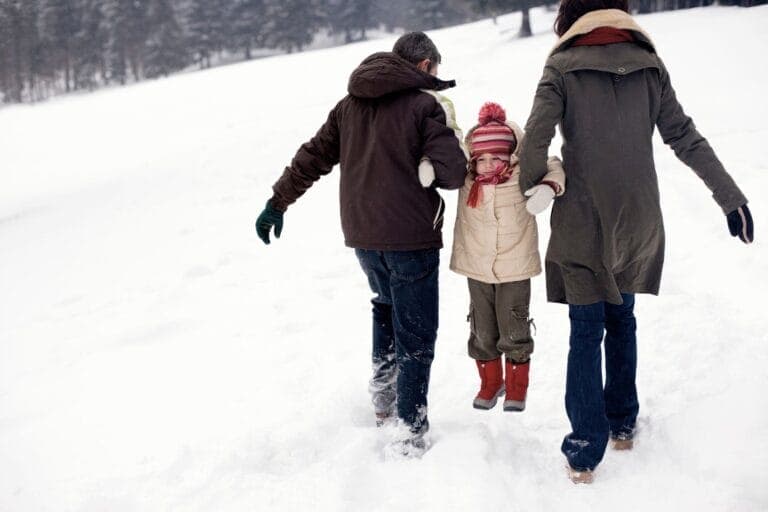 Zwei Erwachsene tragen ein Kind durch den Schnee. Winterferien - das etwas andere Sportprogramm für Eltern.
