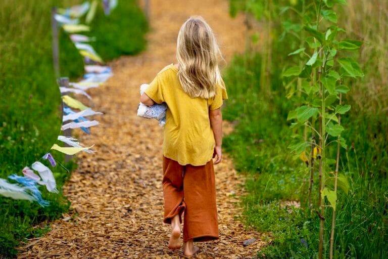 Ein Kind geht barfuss einen Weg entlang. Der Weg ist mit Fähnchen geschmückt. Nadja Schnetzlers Hands-off-Philosophie und Identitätssuche.