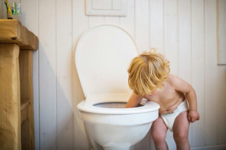 Blondes Kleinkind, nur mit Windel bekleidet, greift mit der Hand in eine Toilettenschüssel. - Trocken werden? Nichts schwieriger als das!